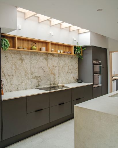 Grey kitchen units with white worktop. Overhead light streams in from the glazed ceiling